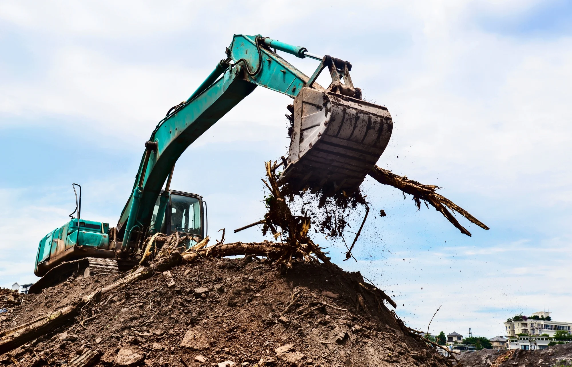 An excavator lifts a large amount of dirt and debris during land clearing.